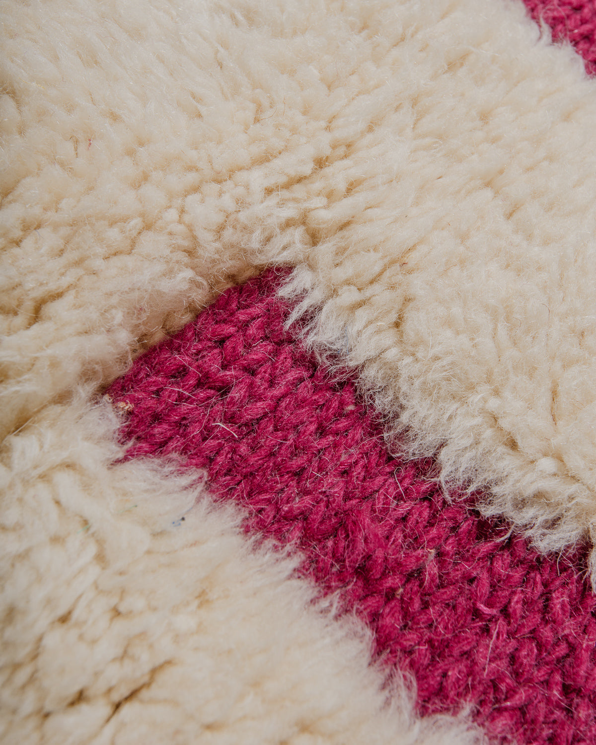 Close-up of a textured cream and magenta geometric patterned rug.